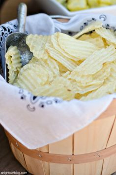 a wooden basket filled with chips next to a bowl of pickles