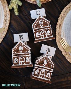 three gingerbread houses are sitting on a table with place cards in front of them