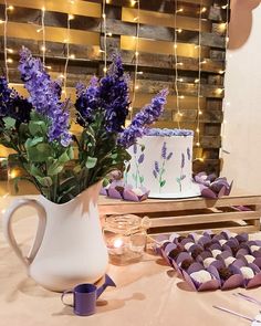 a table topped with purple flowers next to a cake and cupcakes