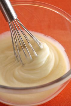 a whisk in a glass bowl filled with white liquid on an orange tablecloth