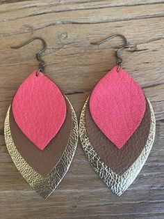 the pink and brown leather earrings are hanging from metal hooks on a wooden surface,