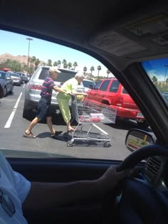 a man pushing a shopping cart through a parking lot with another person in the car