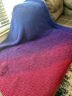 a pink and blue blanket sitting on top of a couch next to a window with blinds