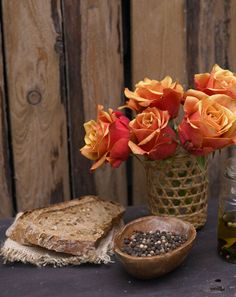 flowers in a vase next to bread and olive oil on a table with wood planks