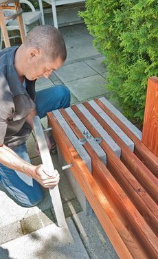 a man is working on some wooden benches in the yard with his hands and nails