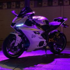 a white and black motorcycle parked in front of a building with purple lights on it