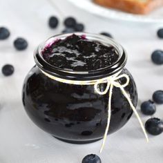 a jar filled with blueberry jam sitting on top of a table next to bread