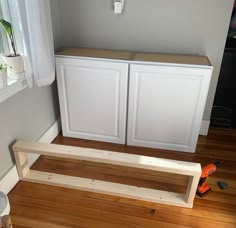 a white cabinet sitting on top of a hard wood floor next to a wooden shelf