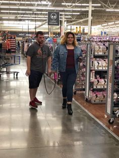 a man and woman are walking in the aisle of a store with their dog on a leash