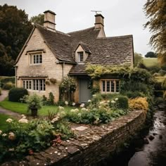 an old house with flowers and plants around the front door is next to a stream