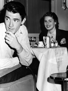 black and white photograph of two people sitting at a table with drinks in front of them