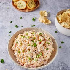 a bowl filled with tuna salad next to chips and crackers on a table top