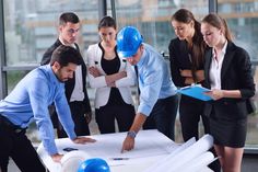 a group of people standing around a blueprint on top of a table in an office