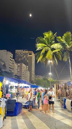 many people are shopping at an open air market in the city with tall buildings and palm trees