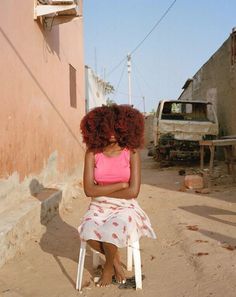 a woman with red curly hair sitting on a chair in the middle of an alleyway