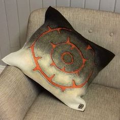 an orange and black pillow sitting on top of a gray couch next to a white wall