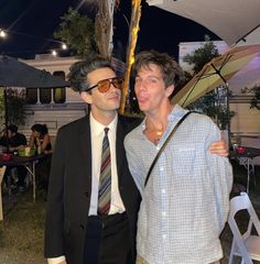 two men standing next to each other in front of an umbrella and building at night