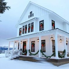 a white house decorated for christmas with wreaths on the front porch and lights hanging from the windows