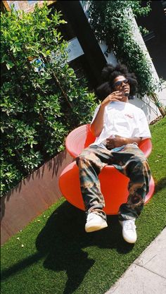 a man sitting on an orange chair talking on his cell phone while wearing sunglasses and camo pants