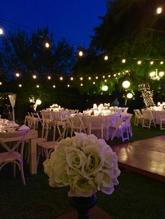 the tables are set with white flowers and lit up lights in the background at night