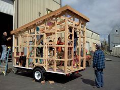 men working on a house being built in the back of a truck with another man standing next to it