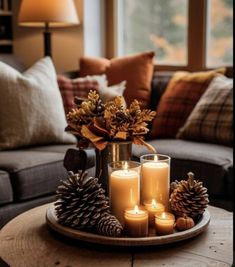 a tray with candles and pine cones on it in front of a couch, window