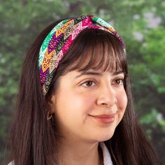 a woman with long hair wearing a colorful headband and smiling at the camera while standing in front of a tree