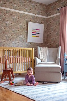 a baby sitting on the floor in front of a crib