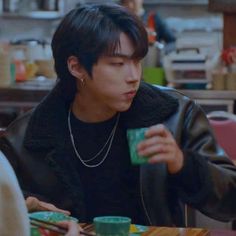 a young man sitting at a table eating food and drinking from a green coffee cup