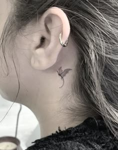 a woman's left ear has a small bird tattoo on it