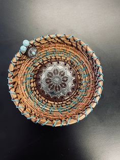 a woven basket is sitting on a black surface with beads and glass bead accents