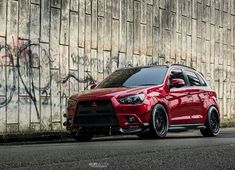 a red car parked in front of a wall with graffiti on it's side