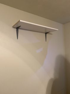 a white shelf hanging on the wall with two metal brackets attached to it's sides