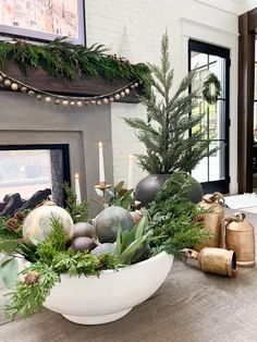 a white bowl filled with christmas decorations on top of a table next to a fireplace