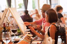 a man and woman sitting at a table in front of an easel with wine glasses on it