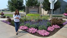 a woman standing in front of a flower bed with purple and pink flowers on it