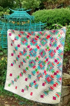 a quilt hanging on a clothes line in the yard with a birdcage behind it