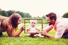 a man, woman and baby are laying in the grass with a picture frame on their chest