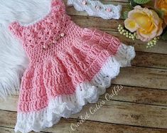 a pink and white crocheted dress next to flowers on a wooden floor with fur