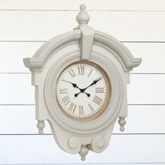 a white clock hanging from the side of a wall with wood planks behind it