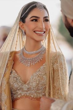 a woman in a bridal gown smiles as she stands next to a man wearing a turban