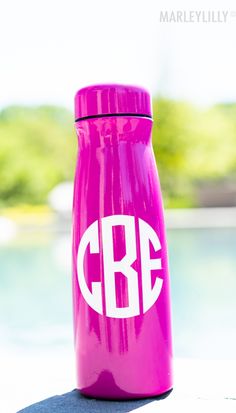 a pink water bottle sitting on top of a table next to a swimming pool and trees