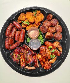 a platter filled with different types of meats and dipping sauce on top of it