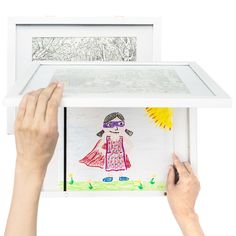 two hands holding up a drawing in front of a white box with drawings on it