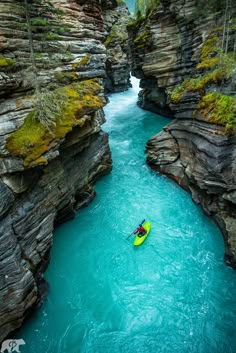 a person in a yellow kayak paddling down a river between two rocky cliffs