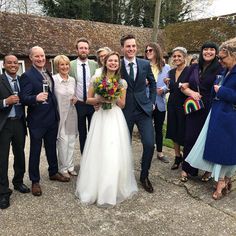 a group of people standing next to each other in front of a building with a bride and groom