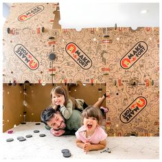 two children and an adult laying on the floor in front of a wall with stickers