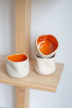 two bowls are sitting on a shelf next to each other, one orange and the other white