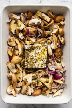 a square white dish filled with mushrooms, onions and other vegetables on a marble counter top