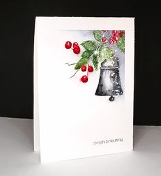 a christmas card with a bell and berries on the front, sitting on a table